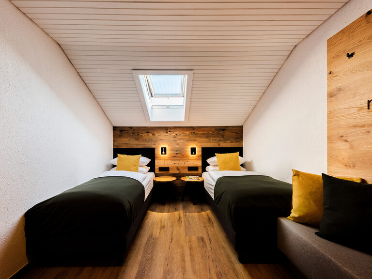 Zwei gemütliche Betten im Holzverkleidungsschlafzimmer im Bodenemais Family & Friends Hotelzimmer im natura Hotel Bodenmais.