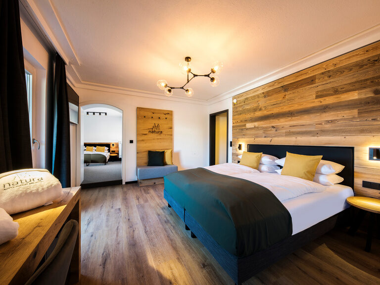 Ein gemütliches Schlafzimmer mit Holzwänden und einladender Einrichtung in der Bodenmais Junior Suite im natura Hotel im Bayerischen Wald.