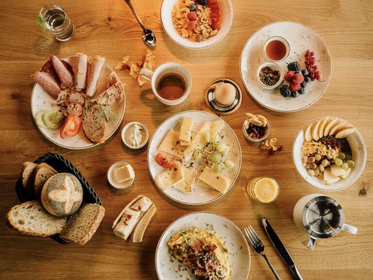 Holztisch mit Frühstücksessen, wie Müsli, Brötchen und weiterem im natura Hotel Bodenmais.