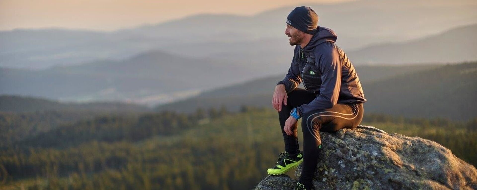Ein Mann sitzt auf einem Berggipfel in der Nähe vom Großen Arber und genießt die Aussicht.