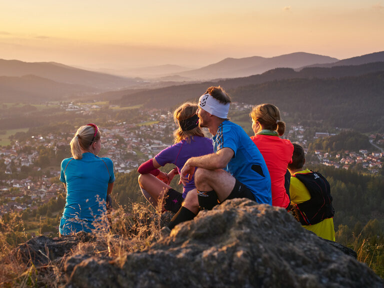 Eine Gruppe von Wanderern sitzt gemeinsam auf einem Gipfel und hat einen tollen Ausblick auf Bodenmais und den Bayerischen Wald.