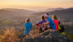 Eine Gruppe von Wanderern sitzt gemeinsam auf einem Gipfel und hat einen tollen Ausblick auf Bodenmais und den Bayerischen Wald.