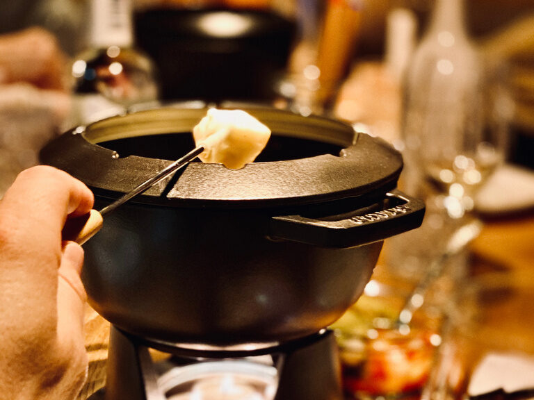 Eine Person hält ein Stück Brot in das Käsefondue im natura Hotel Bodenmais.