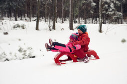 Zwei Kinder fahren gemeinsam auf einem Schlittern in einer Winterlandschaft