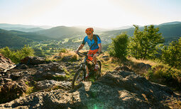 Ein Mann auf einem Mountainbike fährt einen felsigen Pfad im Bayrischen Wald hinunter.