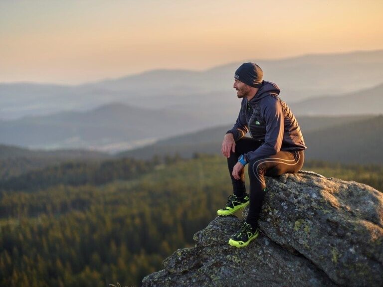Ein Mann sitzt auf einem Berggipfel in der Nähe vom Großen Arber und genießt die Aussicht.