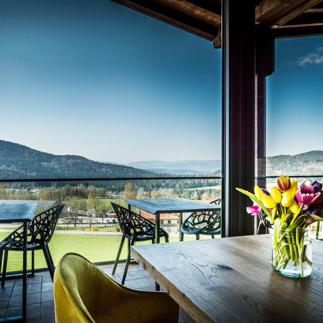 Ein Tisch mit Blumen vor einem großen Fenster mit Panoramablick auf den Bayerischen Wald im natura Hotel Bodenmais.