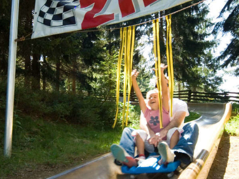 Ein Kind genießt eine Fahrt im Sommerrodelbahn nahe dem natura Familienhotel im Bayerischen Wald
