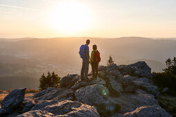 Wanderer pausieren auf einem Gipfel, während sich das Bergpanorama hinter ihnen erstreckt.
