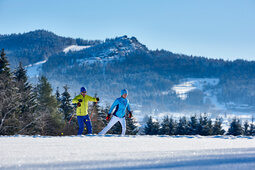 Zwei Langläufer beim Wintersport mit Silberberg im Hintergrund.