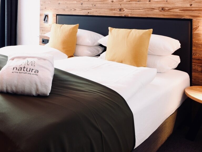 Ein sauber gemachtes Bett mit zwei Kissen im Hotelzimmer des Natura Hotel Bodenmais.